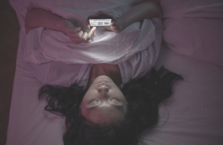 Entspannung zum Einschlafen - Frau mit Blaulicht im Handy im Bett